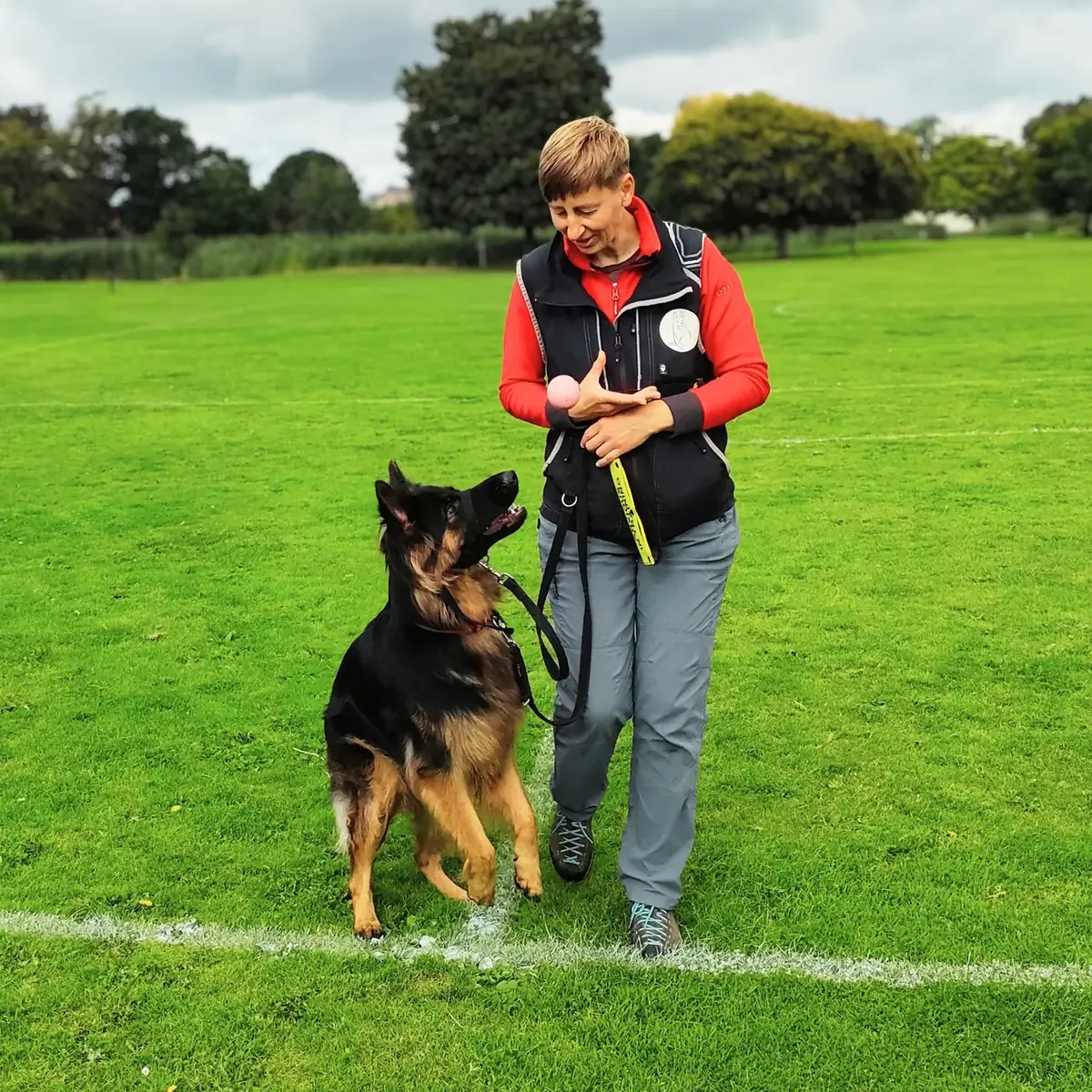 Agata training Nala, a German Shepherd, on a loose lead in an open field